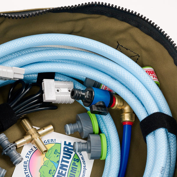 A close-up of coiled blue hoses, metal connectors, two green valve adapters, a power plug, and a sticker inside an olive green zippered bag.
