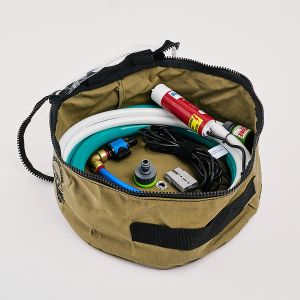 A khaki round zippered bag containing a coiled hose, cables, a red spray can, adapters, and connectors, all neatly arranged inside against a white background.