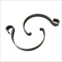 A pair of Awning Tie Down Clips made of dark, curved stainless steel with opposite-facing openings and hook-shaped and straight-cut ends are shown on a white background, ideal for securing roll out awnings.