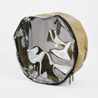 The Adventure Pumps Canvas Bag is a round, handmade canvas bag with a tan body, clear plastic front, and black zipper, shown upright on a white background. Ideal for storing your Adventure Pumps.